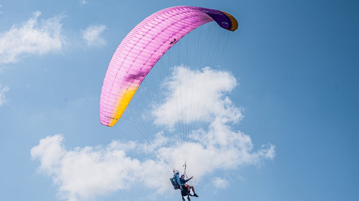 Experience the thrill of tandem paragliding with colorful parachute soaring high in the clear blue sky.